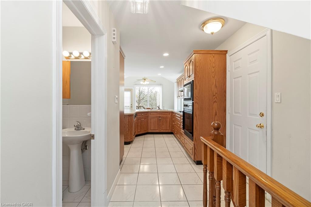 Kitchen with warm wood cabinetry and tiled floor, viewed past a bathroom doorway and stair railing.