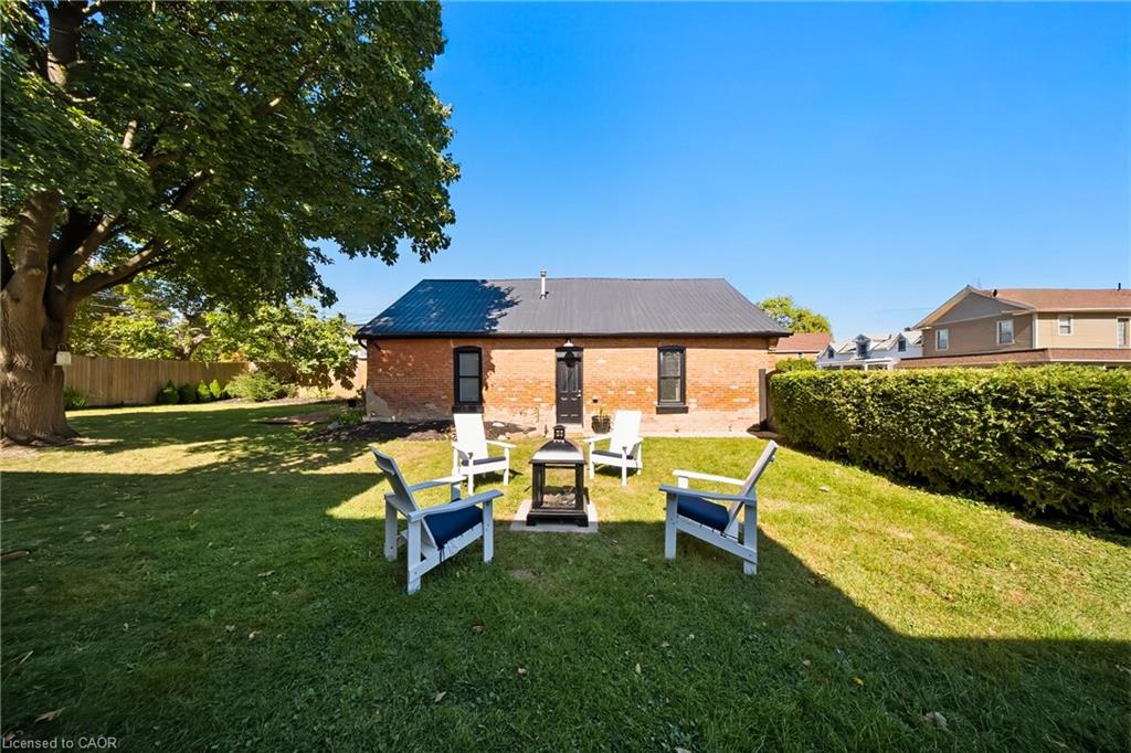 Brick house behind a lawn seating area with chairs around a fire pit and a large shade tree.