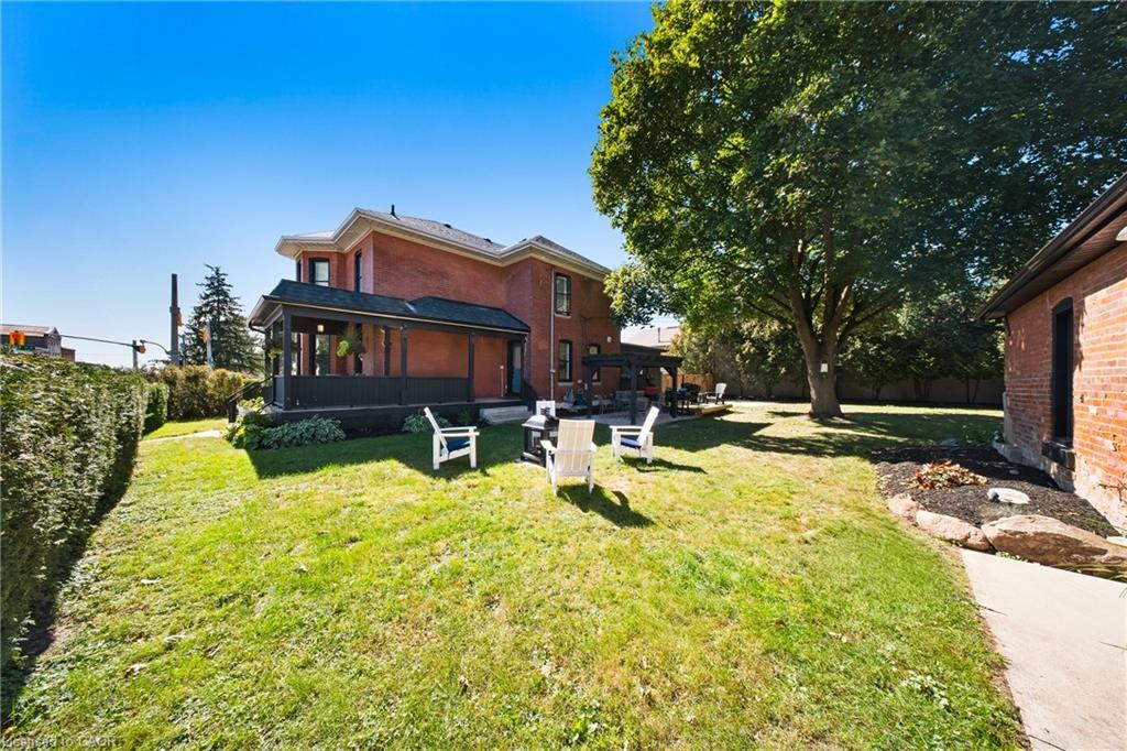 Brick house backyard with a covered porch, lawn chairs, and a large shade tree.
