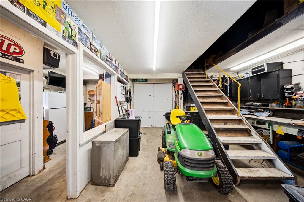 Workshop with a green riding mower, workbenches, and a staircase with yellow handrails.