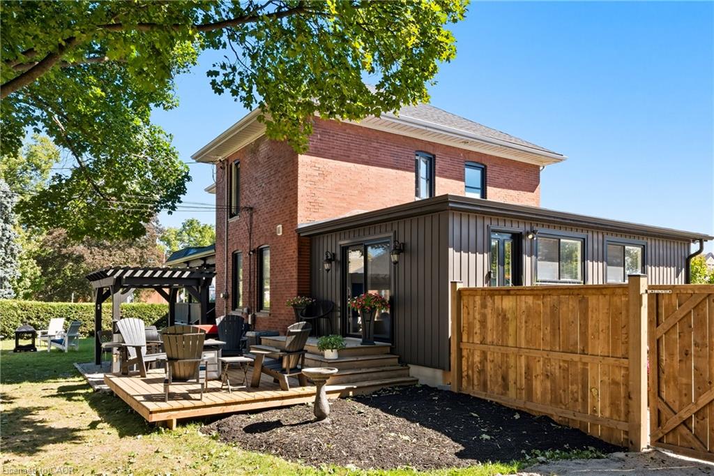 Red-brick house with a dark-sided addition, raised deck, pergola, and fenced backyard.