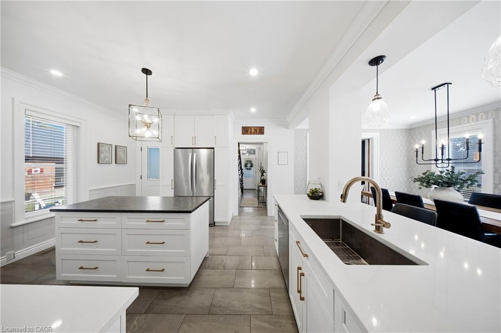 Bright white kitchen with two islands, a stainless-steel refrigerator, gray tile floors, and brass fixtures.