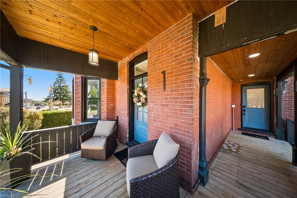 Brick-fronted porch with blue entry doors, wicker chairs, and a wood-plank ceiling.