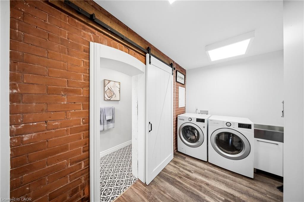 Laundry room with front-loading washer and dryer beside a red brick wall and sliding barn door.