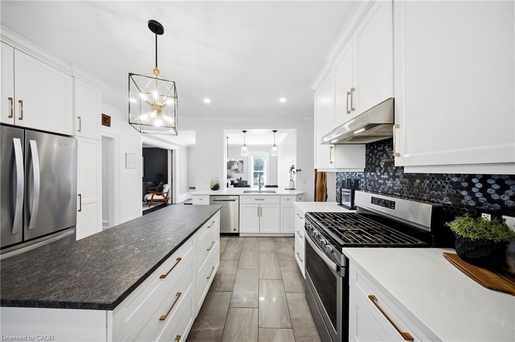 White kitchen with a large gray stone island, stainless-steel range, and black hexagonal backsplash.