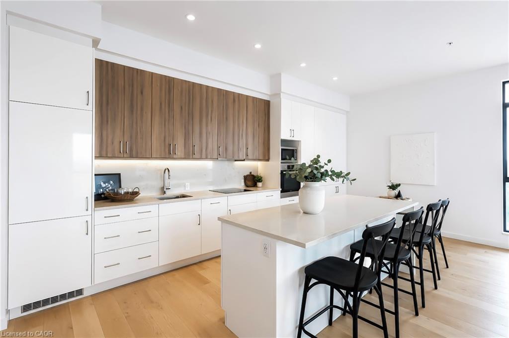 Modern condo kitchen with a large white island, black bar stools, and warm wood cabinetry.