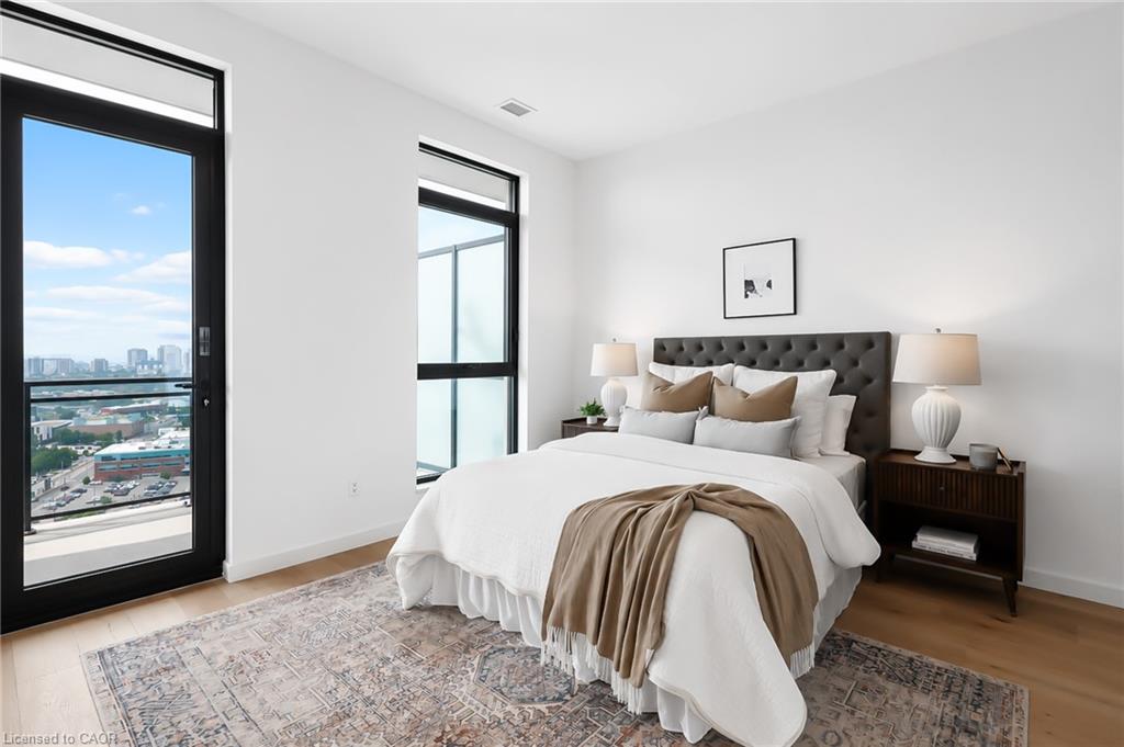 Staged condo bedroom with a white bed, tufted headboard, and tall windows overlooking the city.