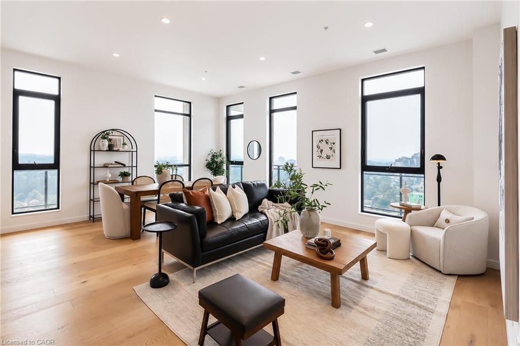 Staged condo living room with a black sofa, dining area, and tall black-framed windows.