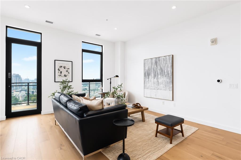 Furnished condo living room with a black leather sofa and tall city-view windows.