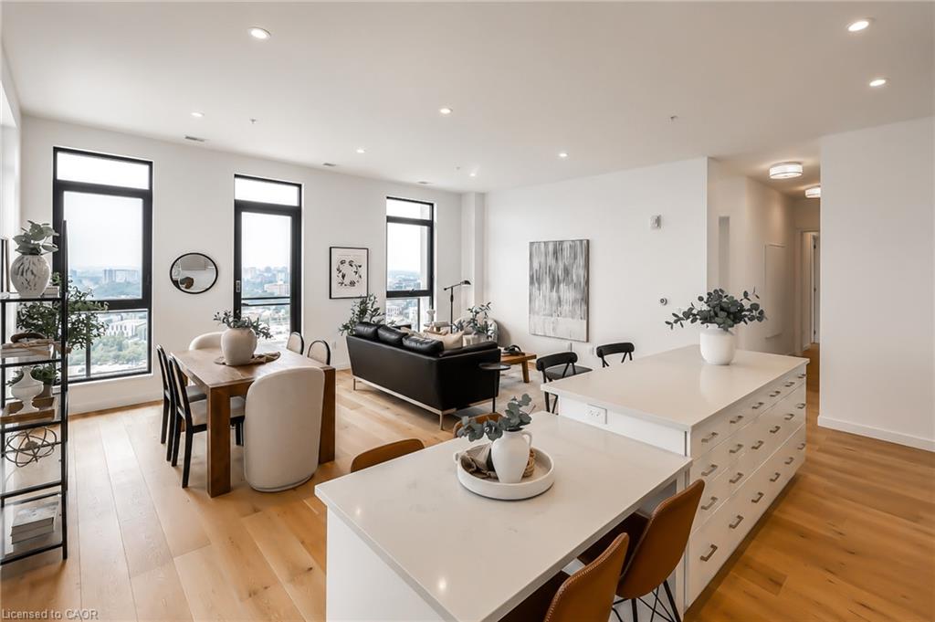 Open-plan condo with a white kitchen island, dining area, black sofa, and city views through tall windows.