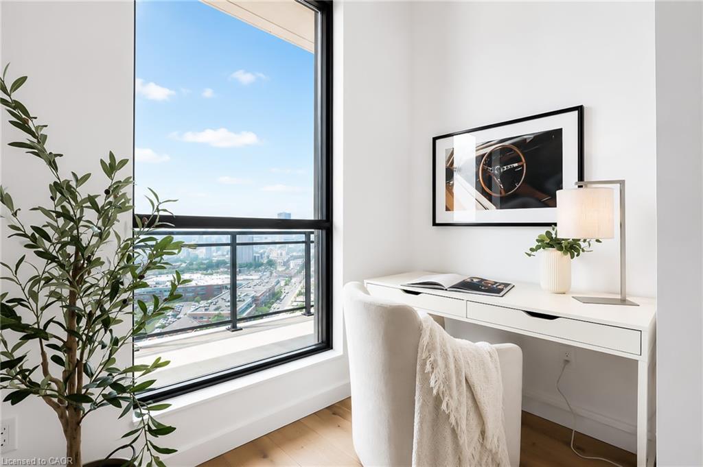 Staged condo office nook with a white desk beside a floor-to-ceiling window overlooking the city.