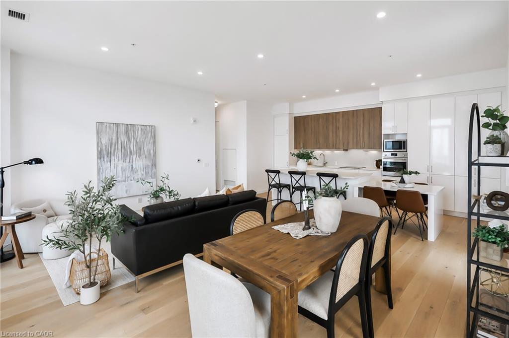 Open-plan condo living and dining area with a modern kitchen, wood cabinetry, and light wood floors.