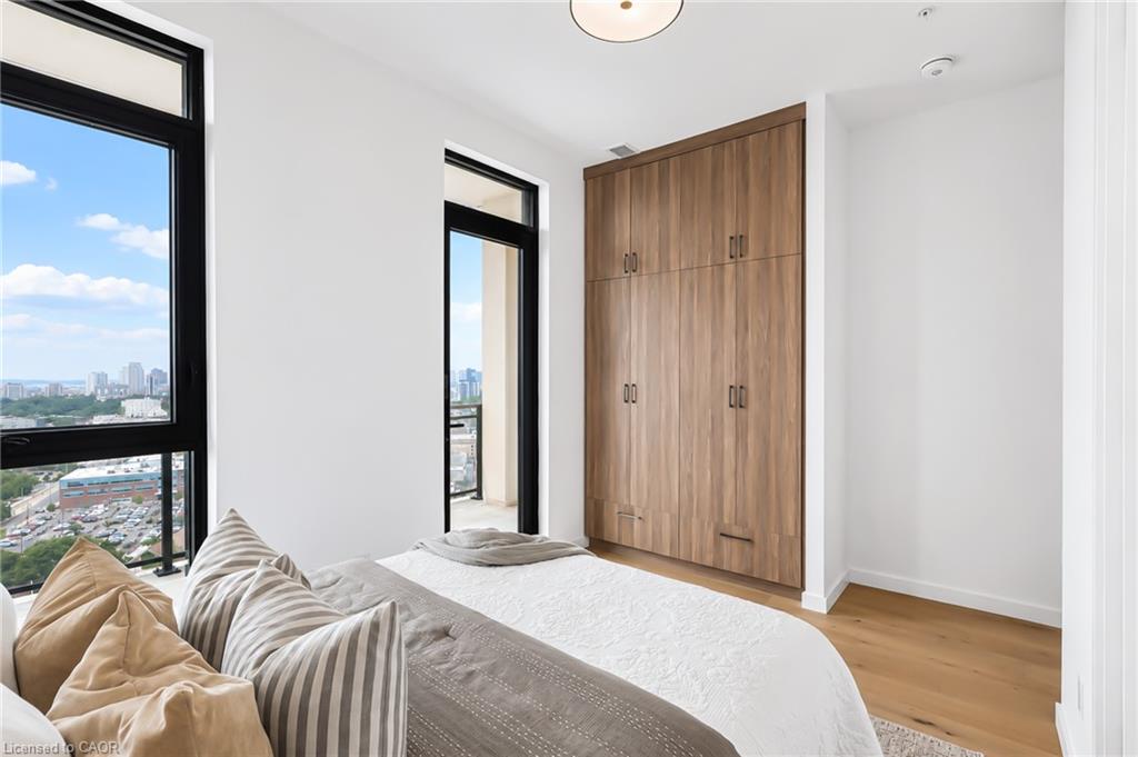 Condominium bedroom with built-in wood wardrobes and large windows overlooking the city.