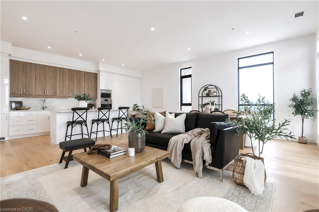 Open-concept condo living room and kitchen with a black sofa, wood coffee table, and large windows.