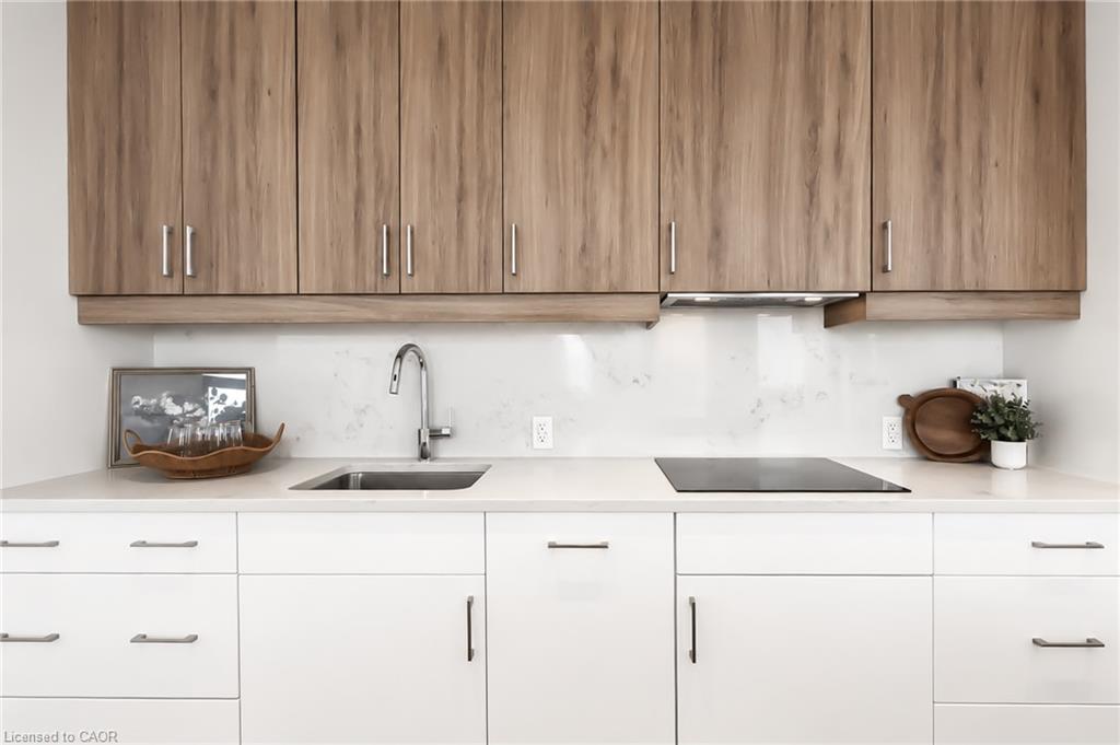 Modern kitchen with light wood upper cabinets, white counters, a stainless sink, and an induction cooktop.