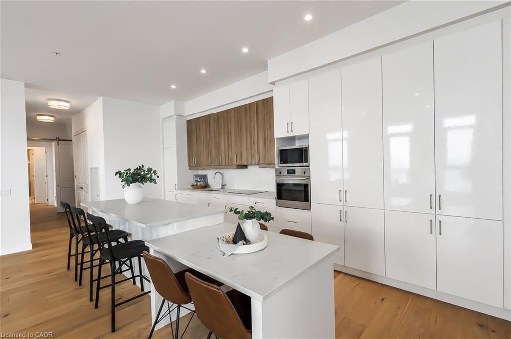 Open-plan condo kitchen with glossy white cabinets, wood accent wall, and a large island with bar seating.