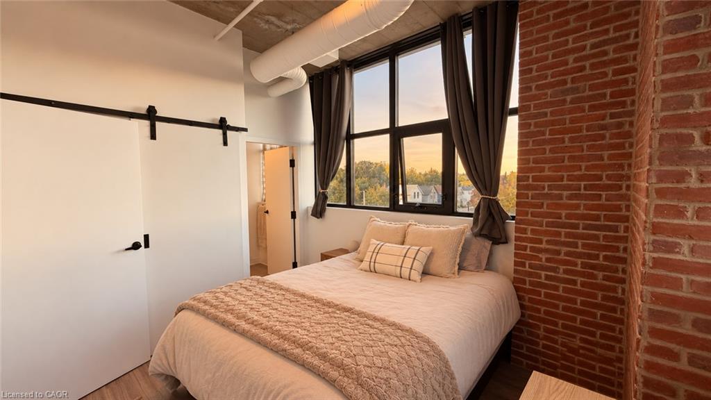 Staged bedroom with a large window, exposed brick wall, and white bedding.