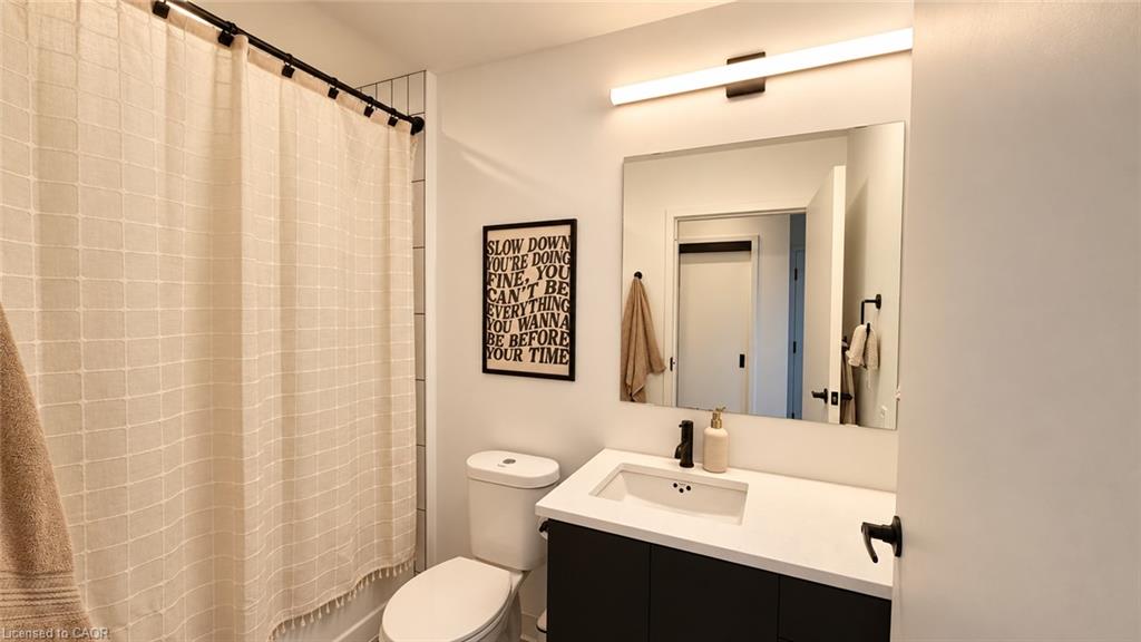 Bathroom with a tiled shower curtain, toilet, and dark vanity beneath a large mirror.