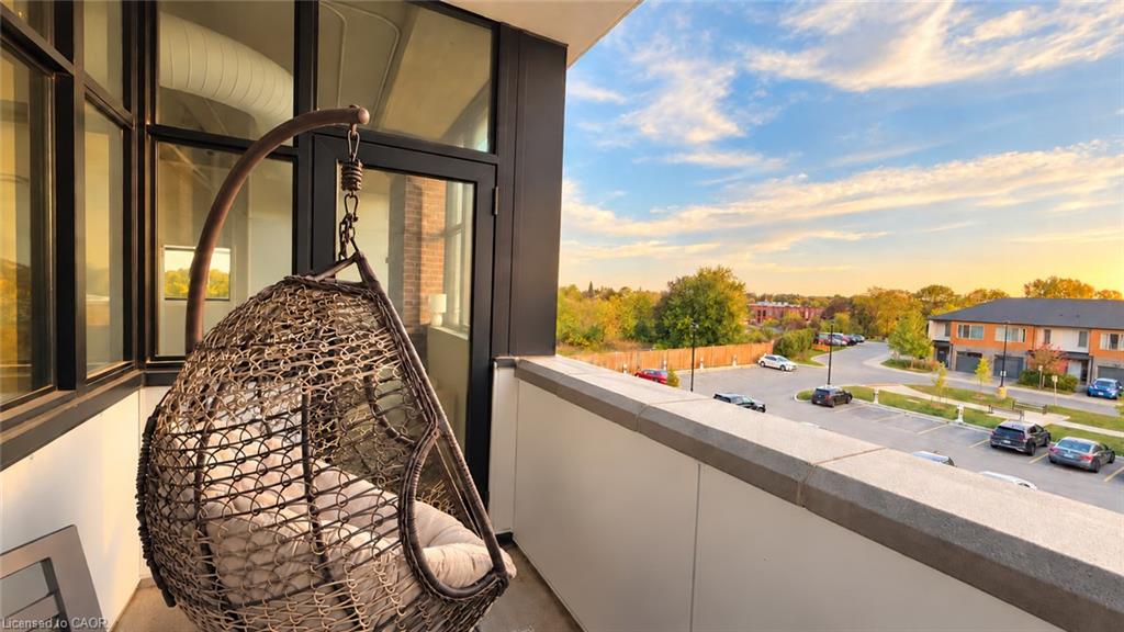 Condo balcony with a hanging wicker chair overlooking a parking lot and tree-lined neighborhood.
