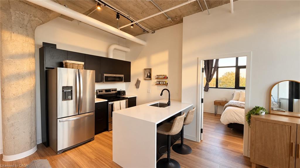 Modern kitchen with a white island, stainless steel appliances, and an open view into the bedroom.