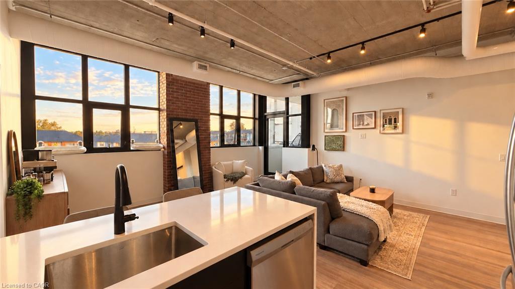 Open-concept kitchen and living area with a white island, exposed brick, and large windows.