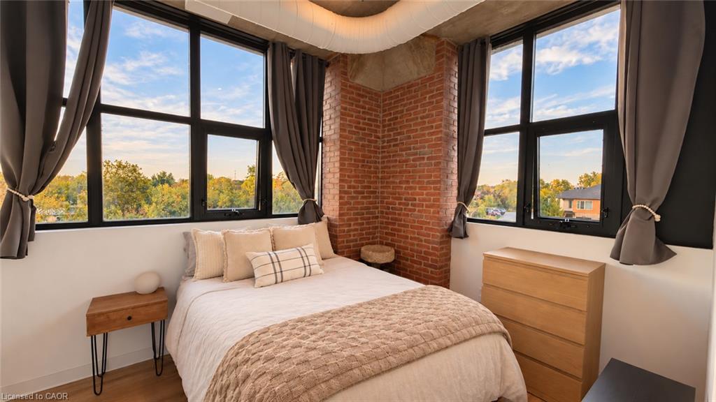 Bedroom with a bed beneath large black-framed windows and an exposed brick corner.