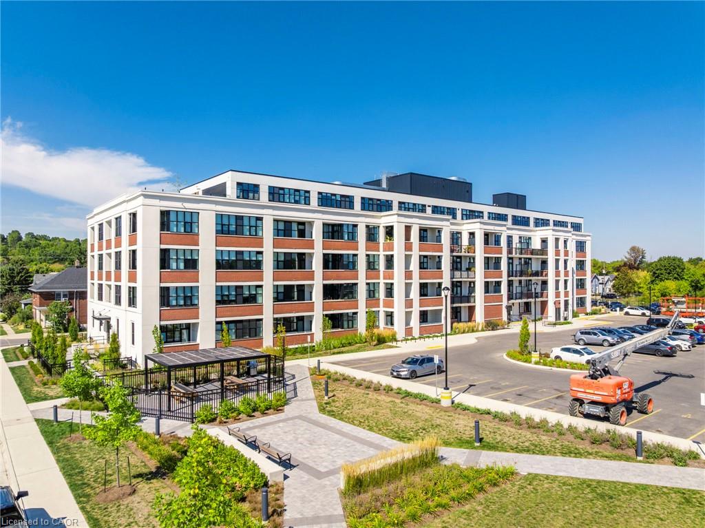 Modern mid-rise condominium with white and brick-red facade, landscaped plaza, and parking lot.