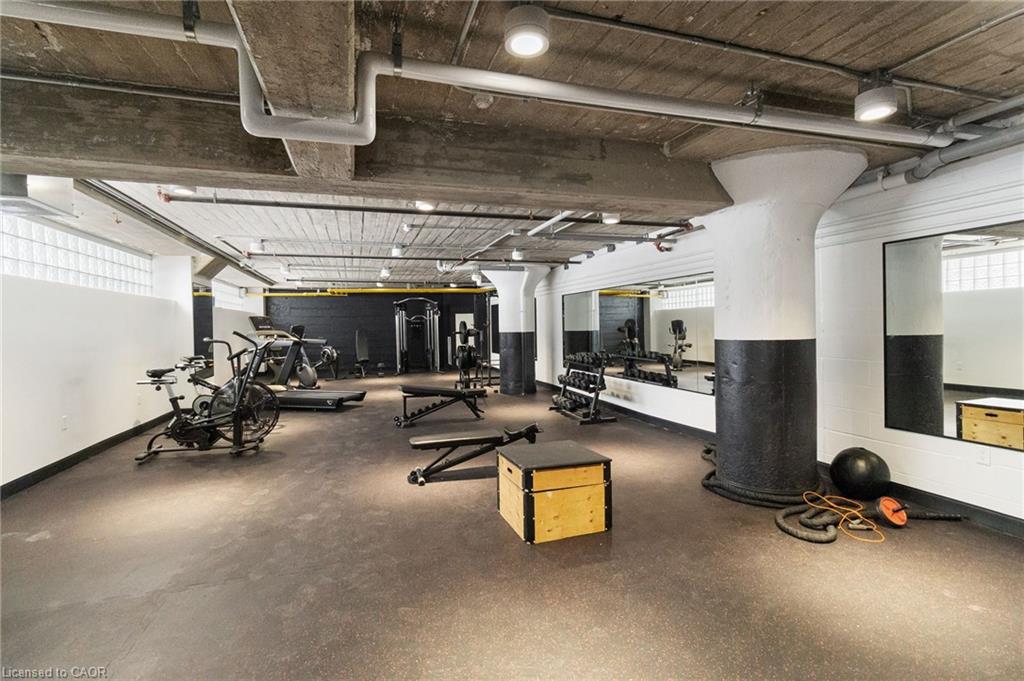 Building fitness room with cardio machines, weights, mirrors, and an exposed concrete ceiling.