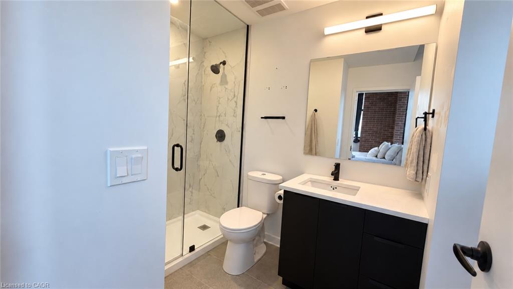 Bathroom with a marble-look glass shower, toilet, and black vanity with a white countertop.