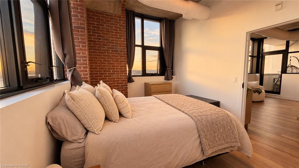 Staged bedroom with a brick accent wall, large black-framed windows, and a quilted throw on the bed.