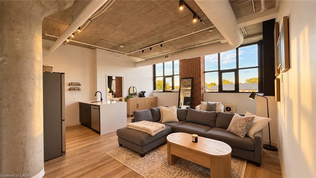Open-concept condo living room and kitchen with exposed concrete ceiling, brick column, and large windows.