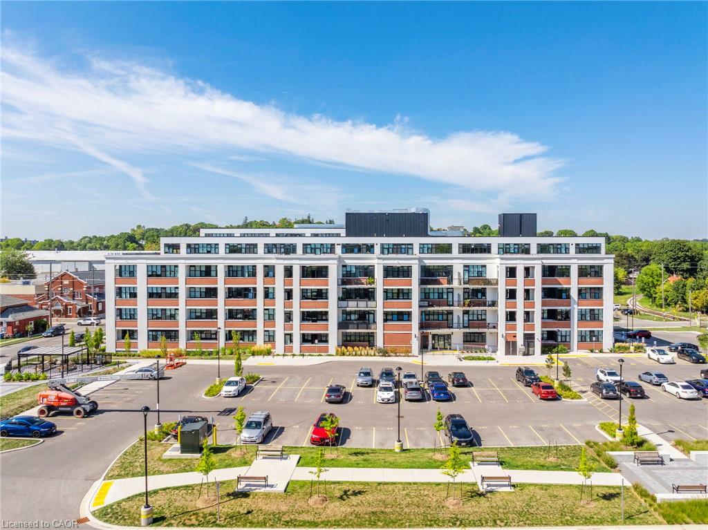 Modern multi-story condominium building with a large parking lot and landscaped walkway in front.
