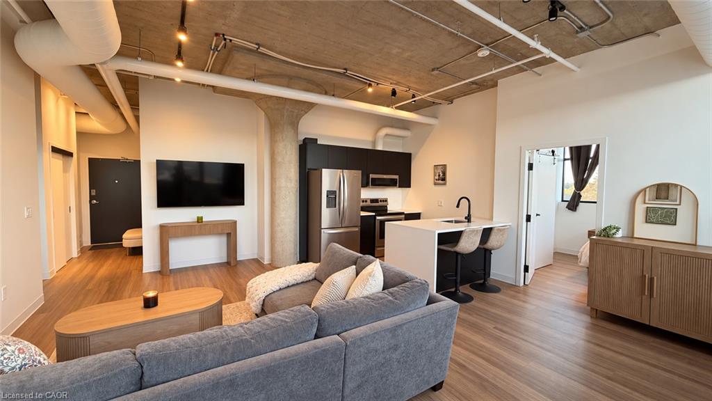 Open-concept living room and kitchen with exposed concrete ceiling and gray sectional sofa.