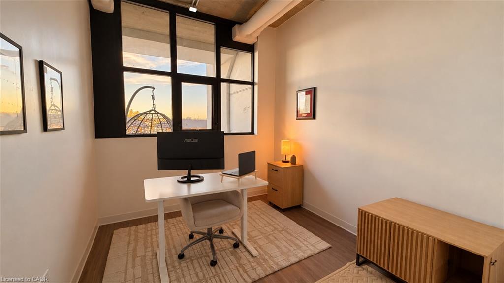 Home office with a white desk and monitor beside tall black-framed windows.