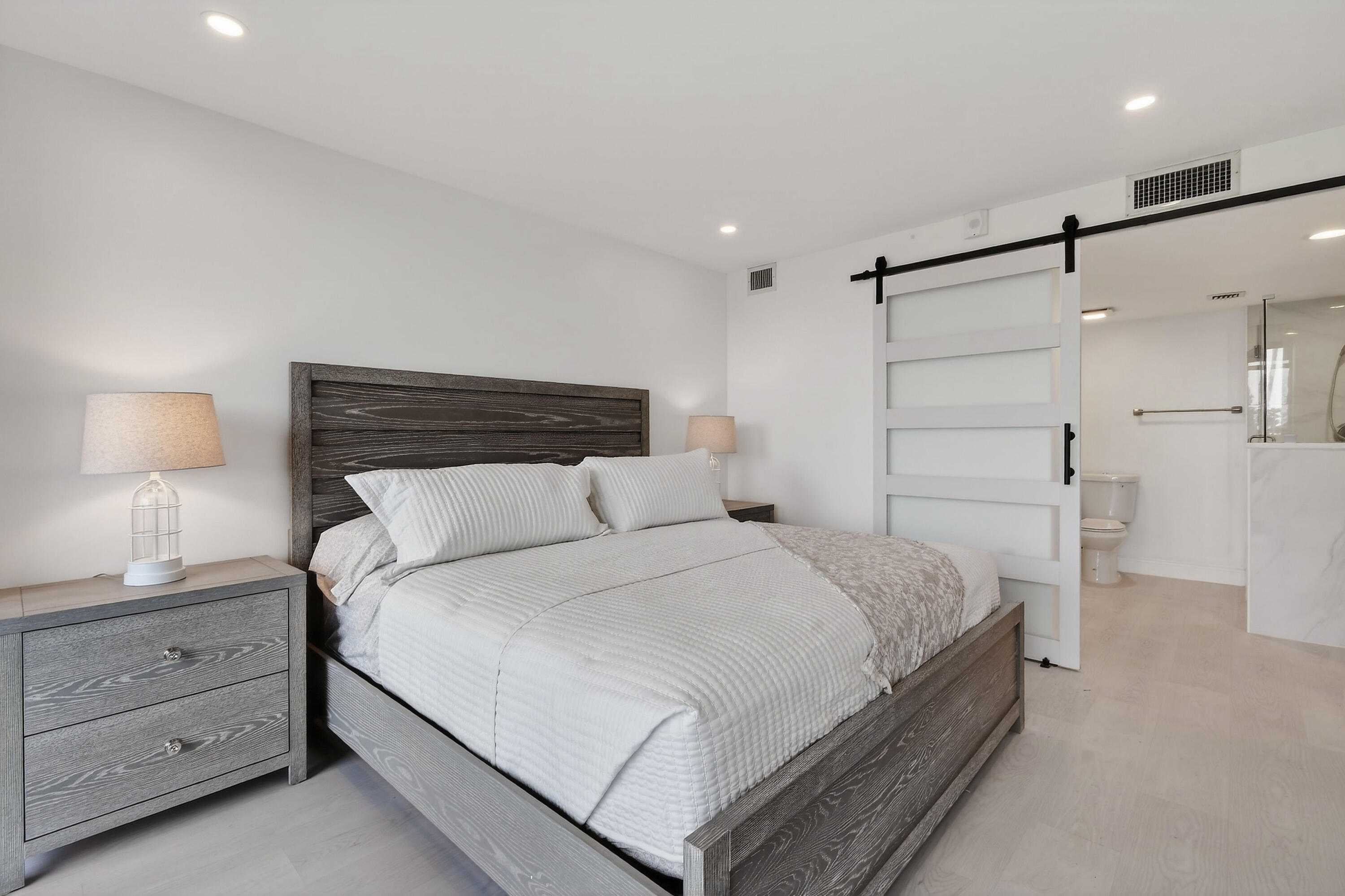 Bedroom with white bedding, a dark wood bed, and a sliding barn door to the bathroom.
