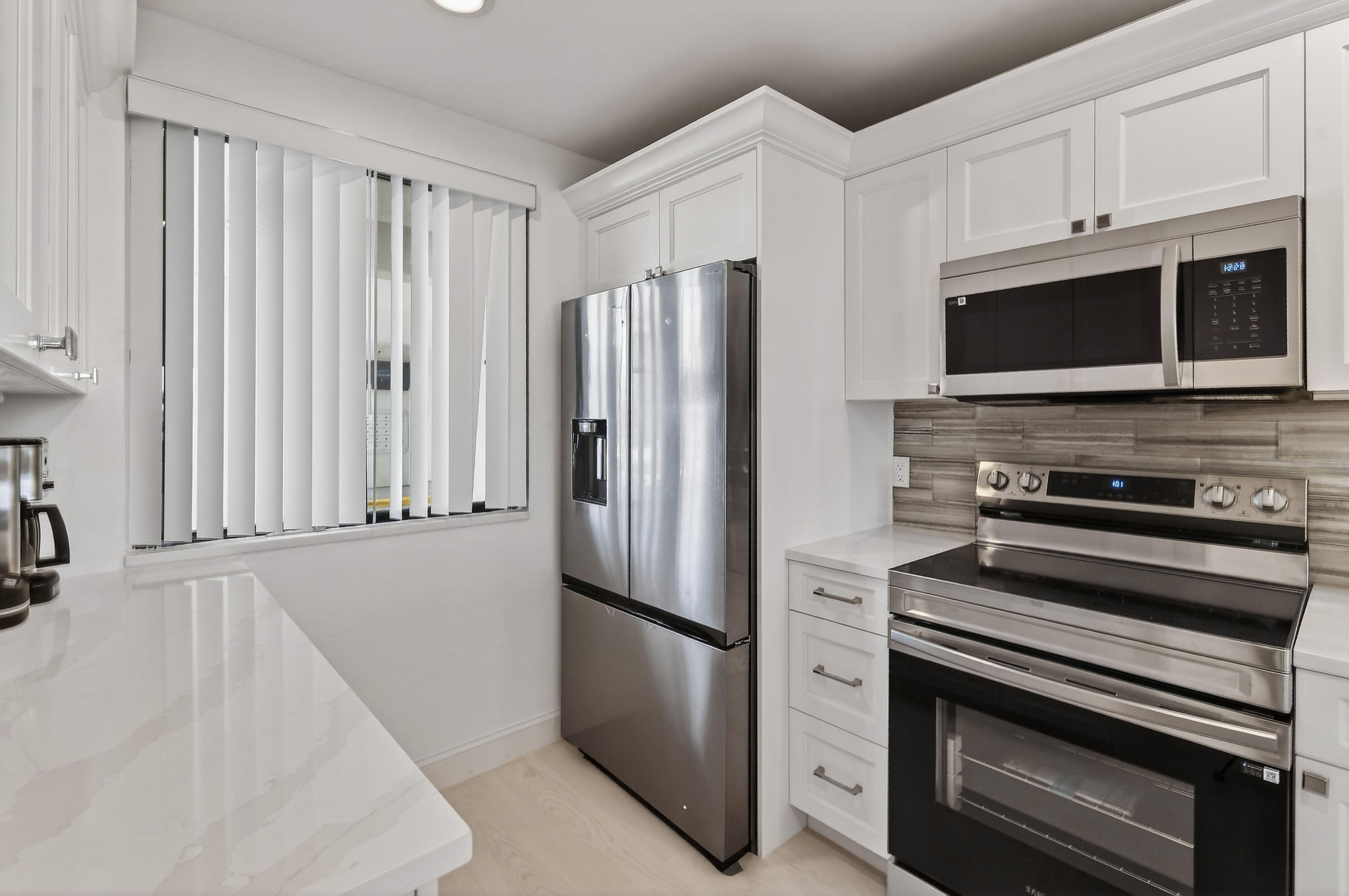 Kitchen with white cabinetry, stainless steel appliances, and a gray tile backsplash.