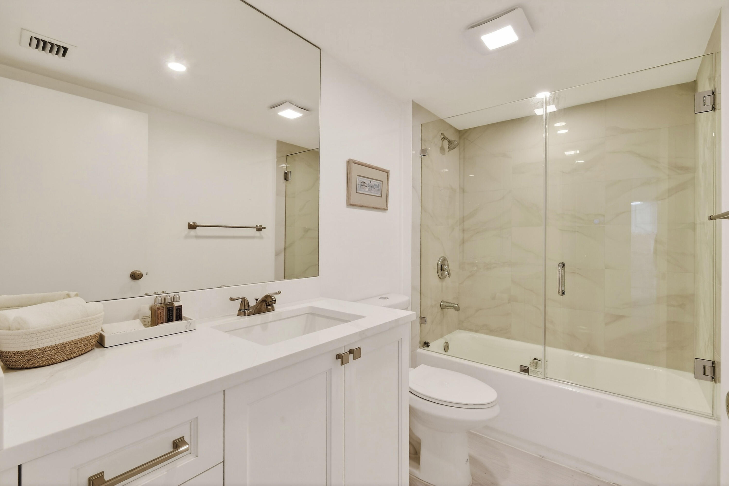 Bathroom with a white vanity, large mirror, and glass-enclosed marble-look tub and shower.