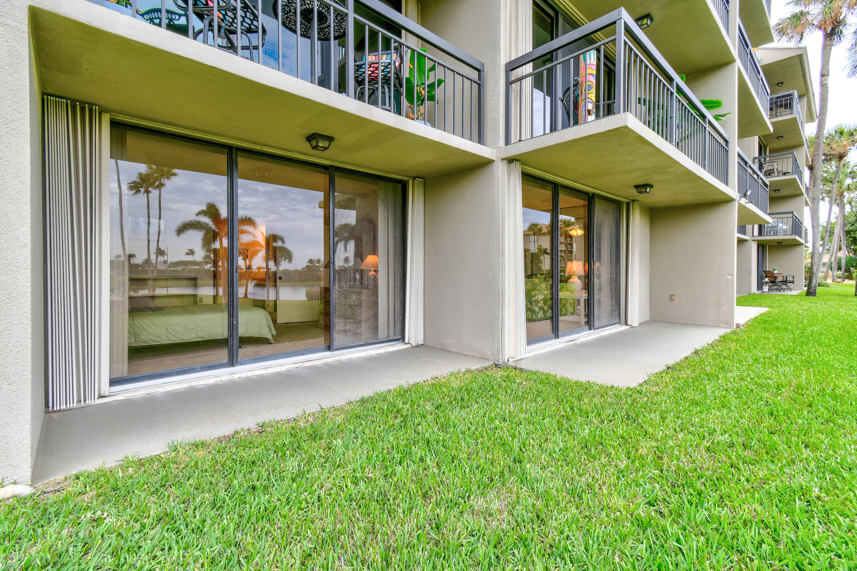 Ground-floor condo patios with sliding glass doors, upper balconies, and a grassy lawn.