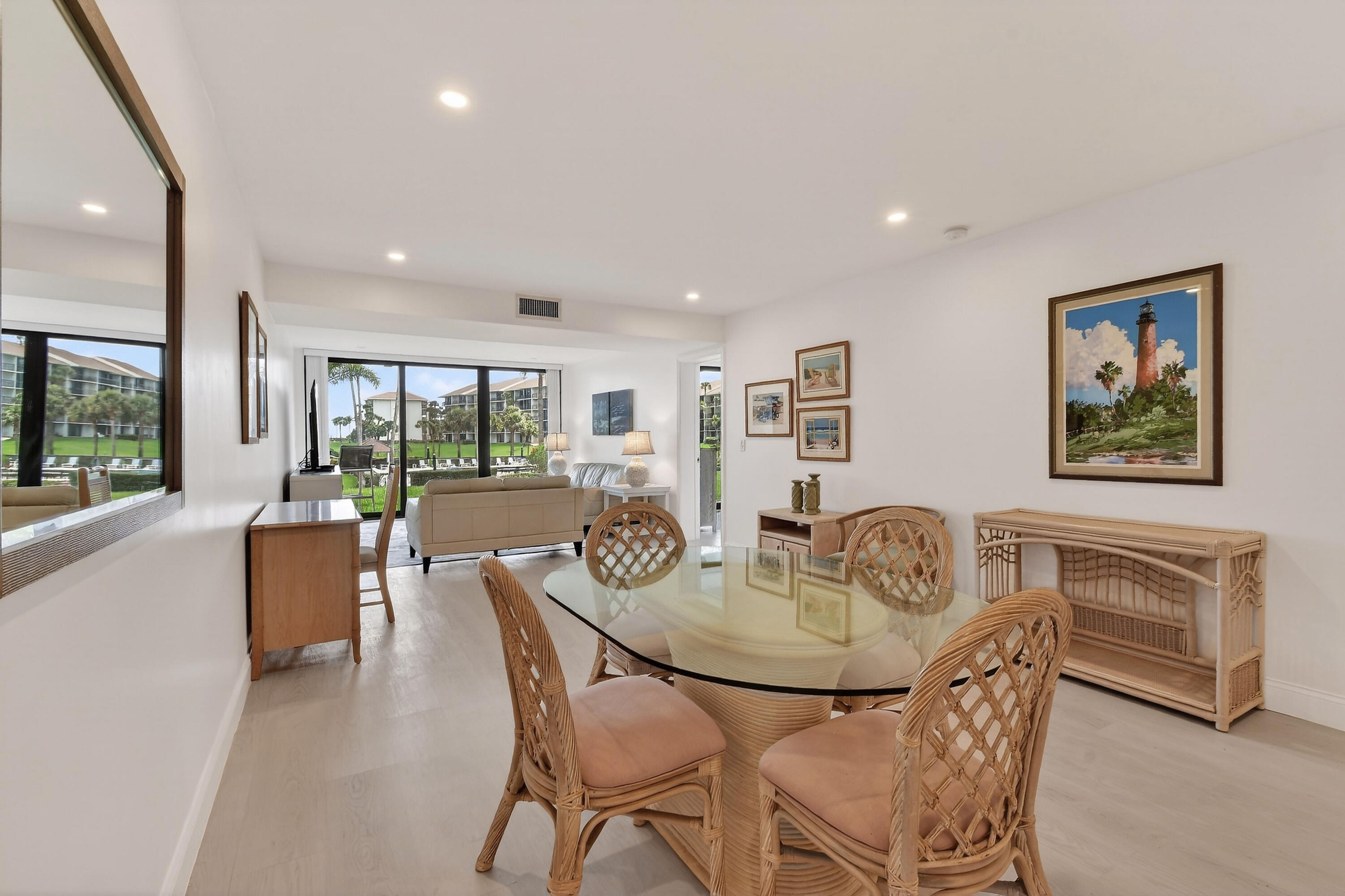 Dining area with a glass-top table and wicker chairs beside sliding doors overlooking landscaped grounds.