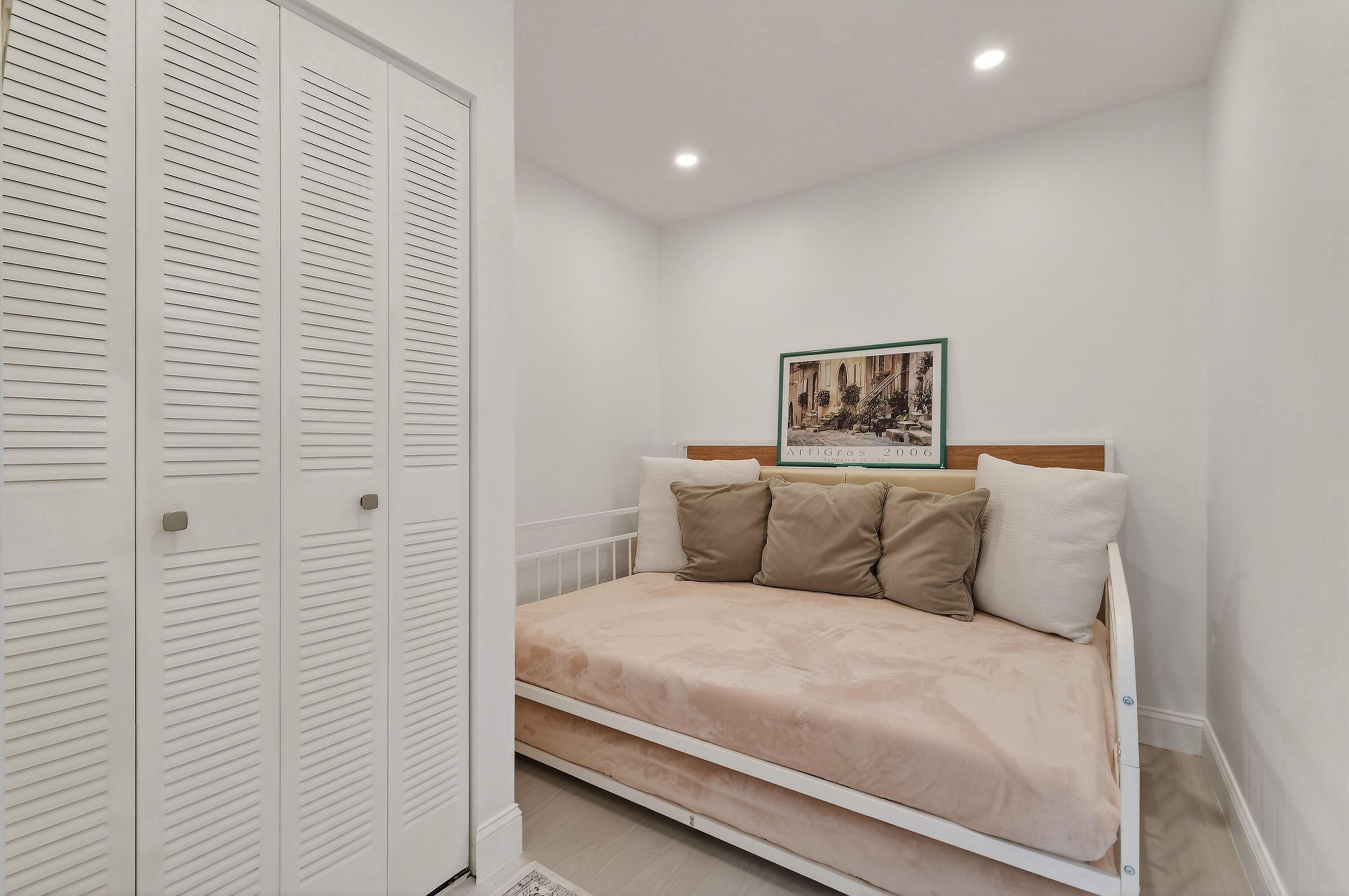 Bedroom with white louvered closets and a beige daybed beneath framed artwork.