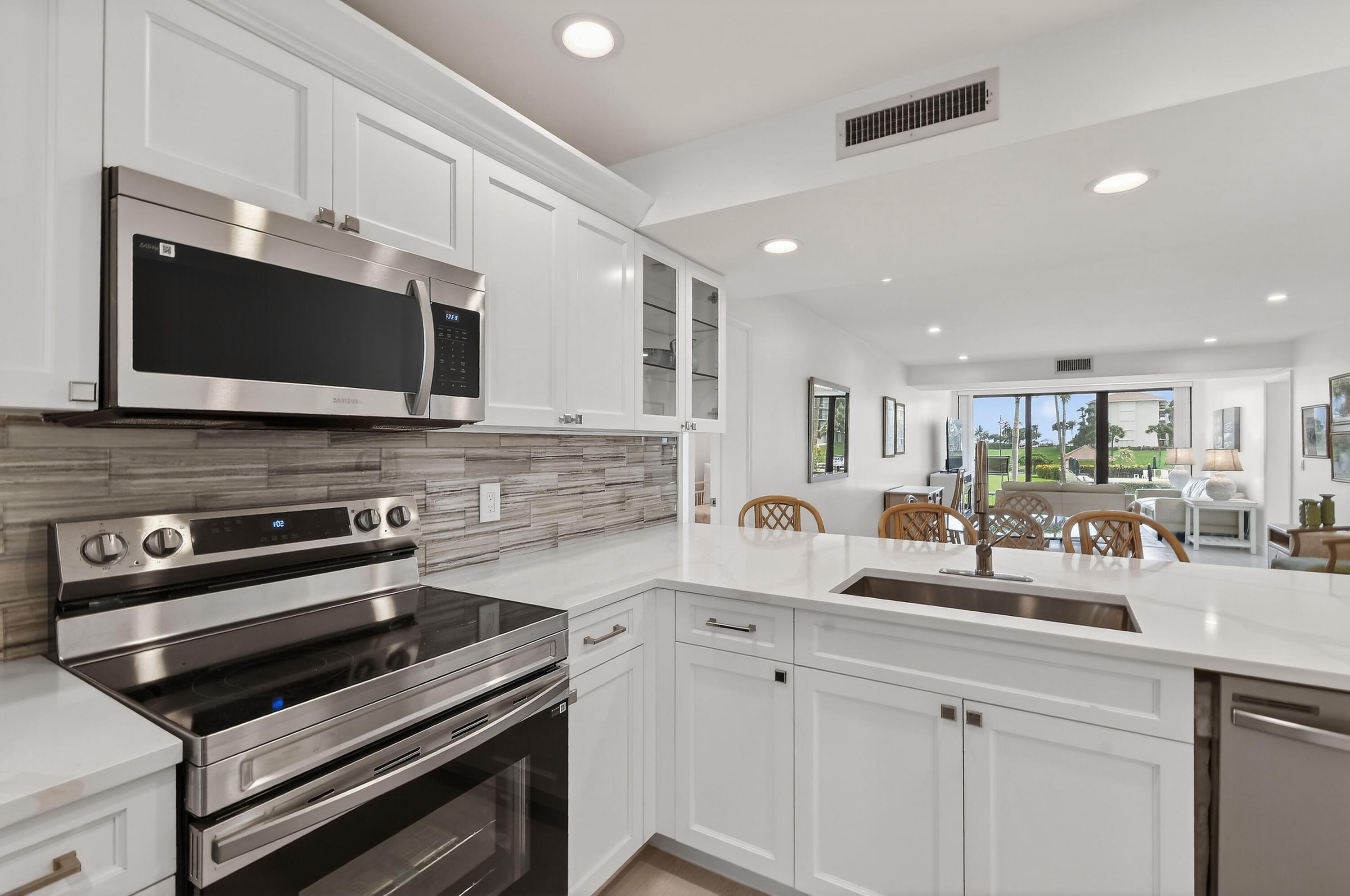 Bright white kitchen with stainless steel appliances and a large island opening onto the living area.