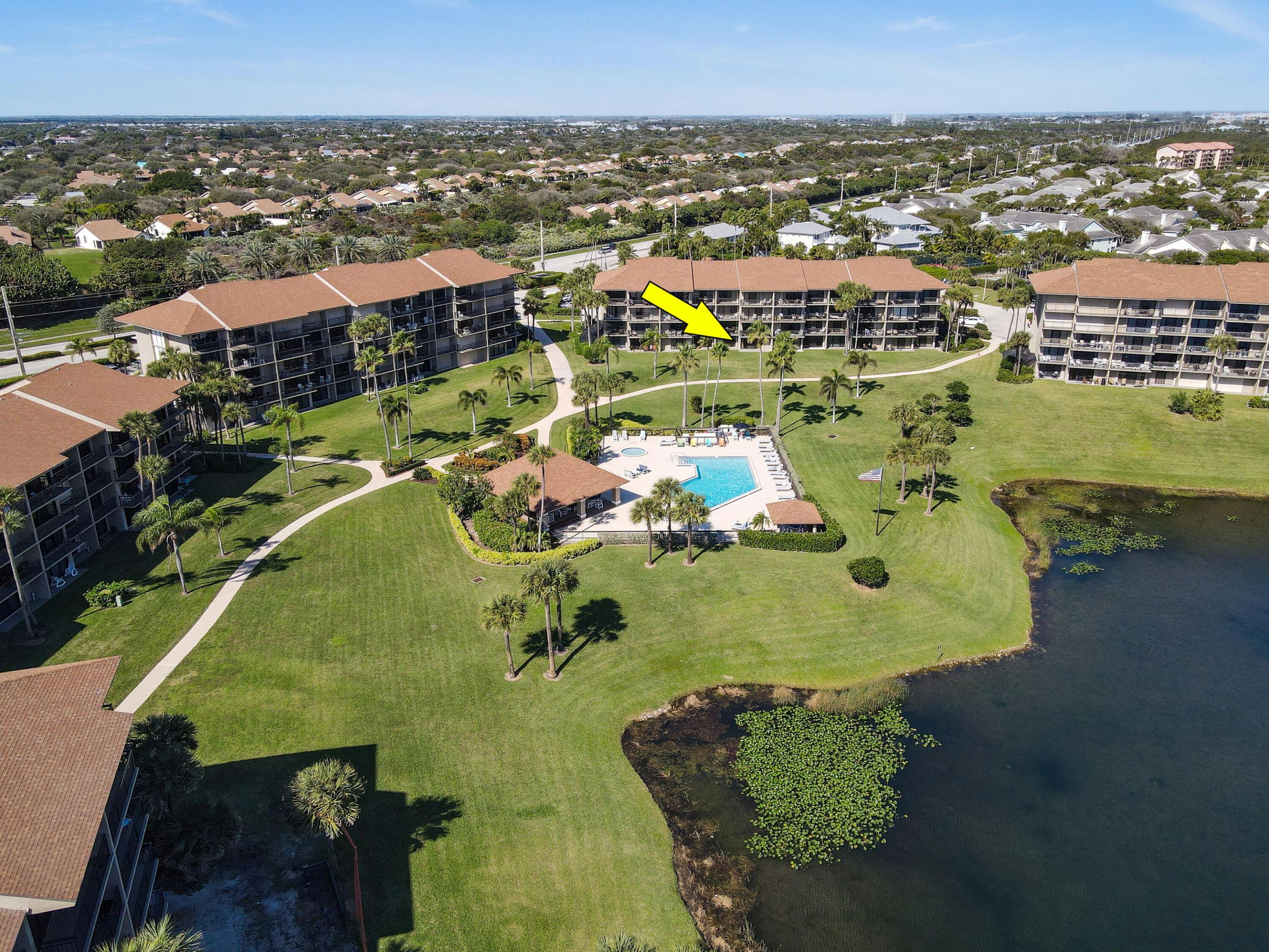 Aerial view of condo buildings, pool, and lakeside grounds; a yellow arrow marks a unit in the central building.