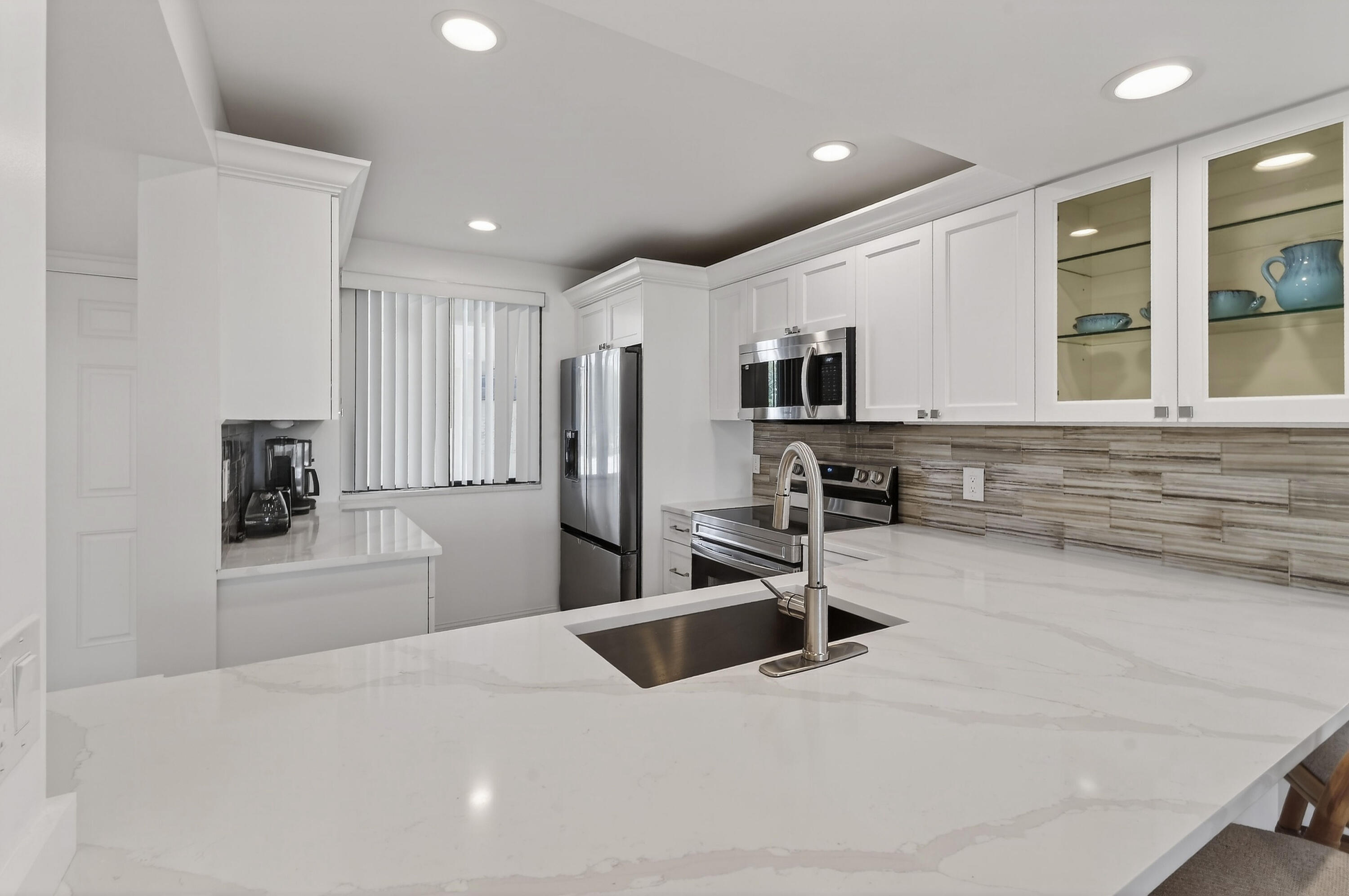 Modern white kitchen with a large island, stainless steel appliances, and wood-look tile backsplash.
