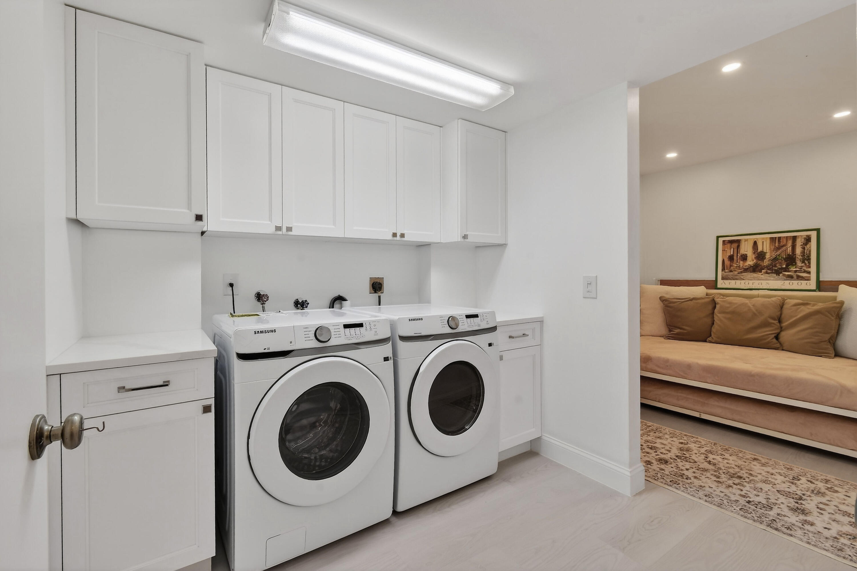 Laundry room with white cabinetry, front-loading washer and dryer, and a view into a sitting area.