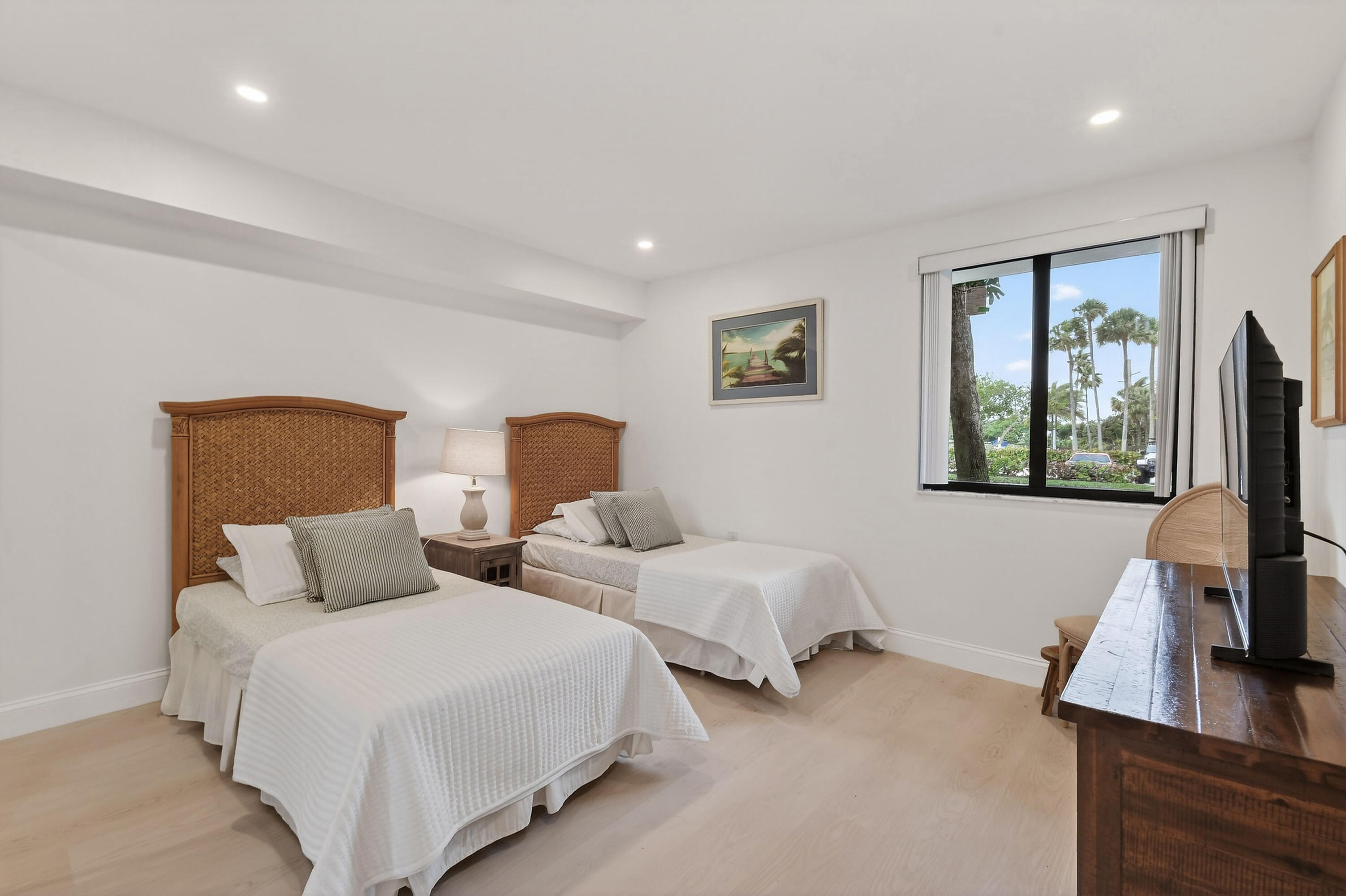 Bedroom with two beds, woven wooden headboards, and a window overlooking palm trees.