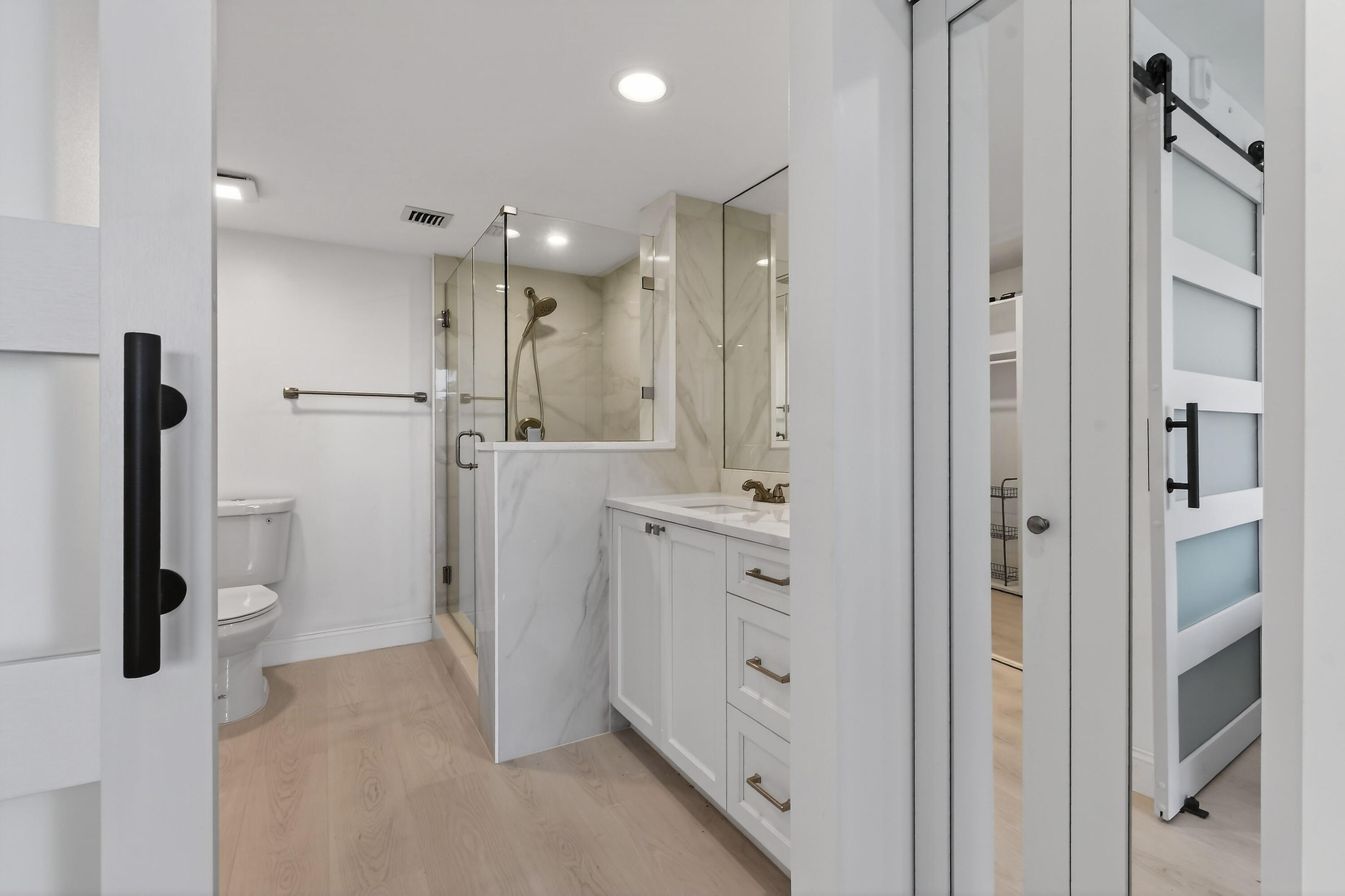 Modern bathroom with glass walk-in shower, white vanity, and light wood flooring.