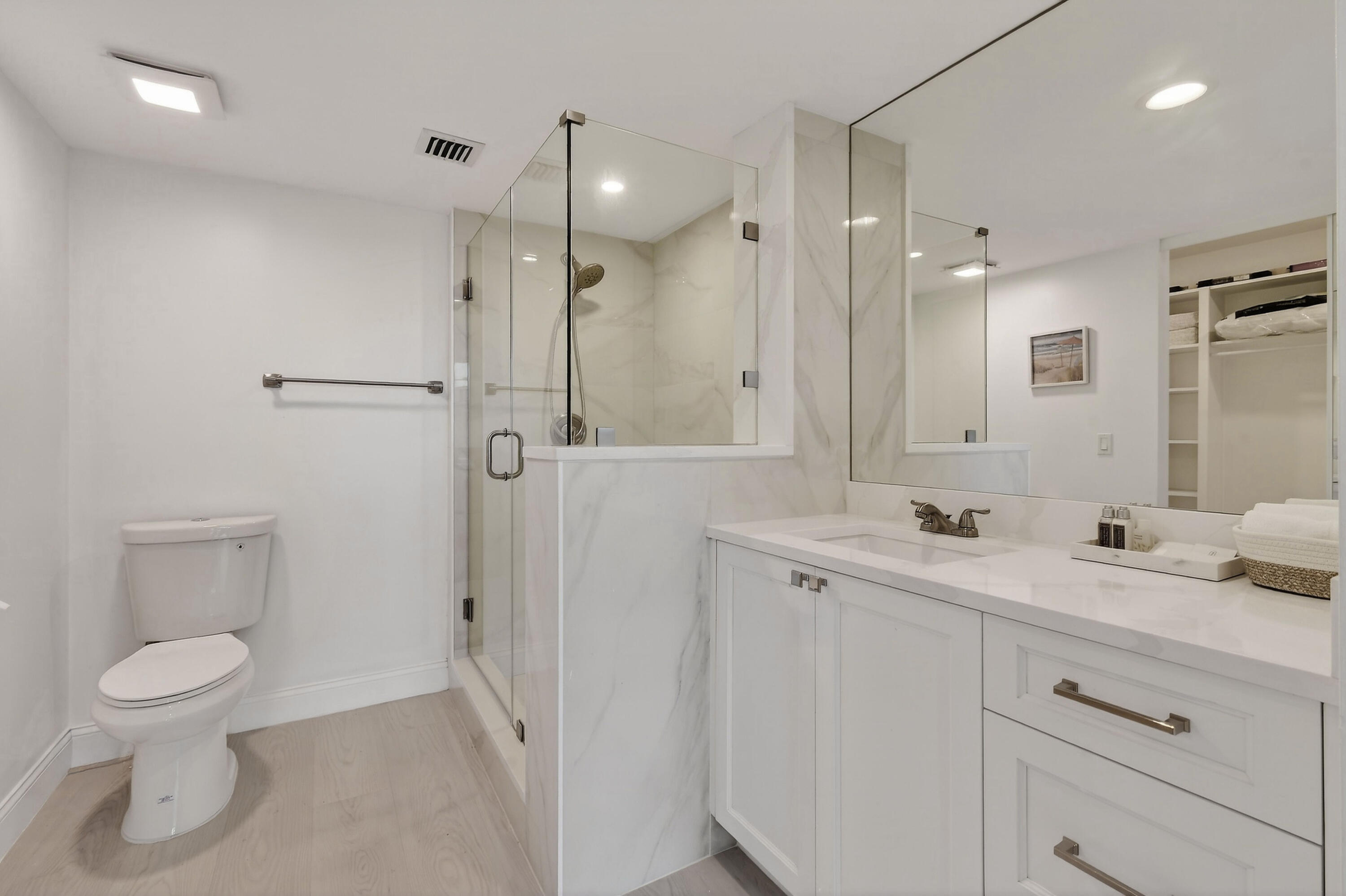 Bathroom with a glass shower, marble-look tile, white vanity, and light wood-look flooring.