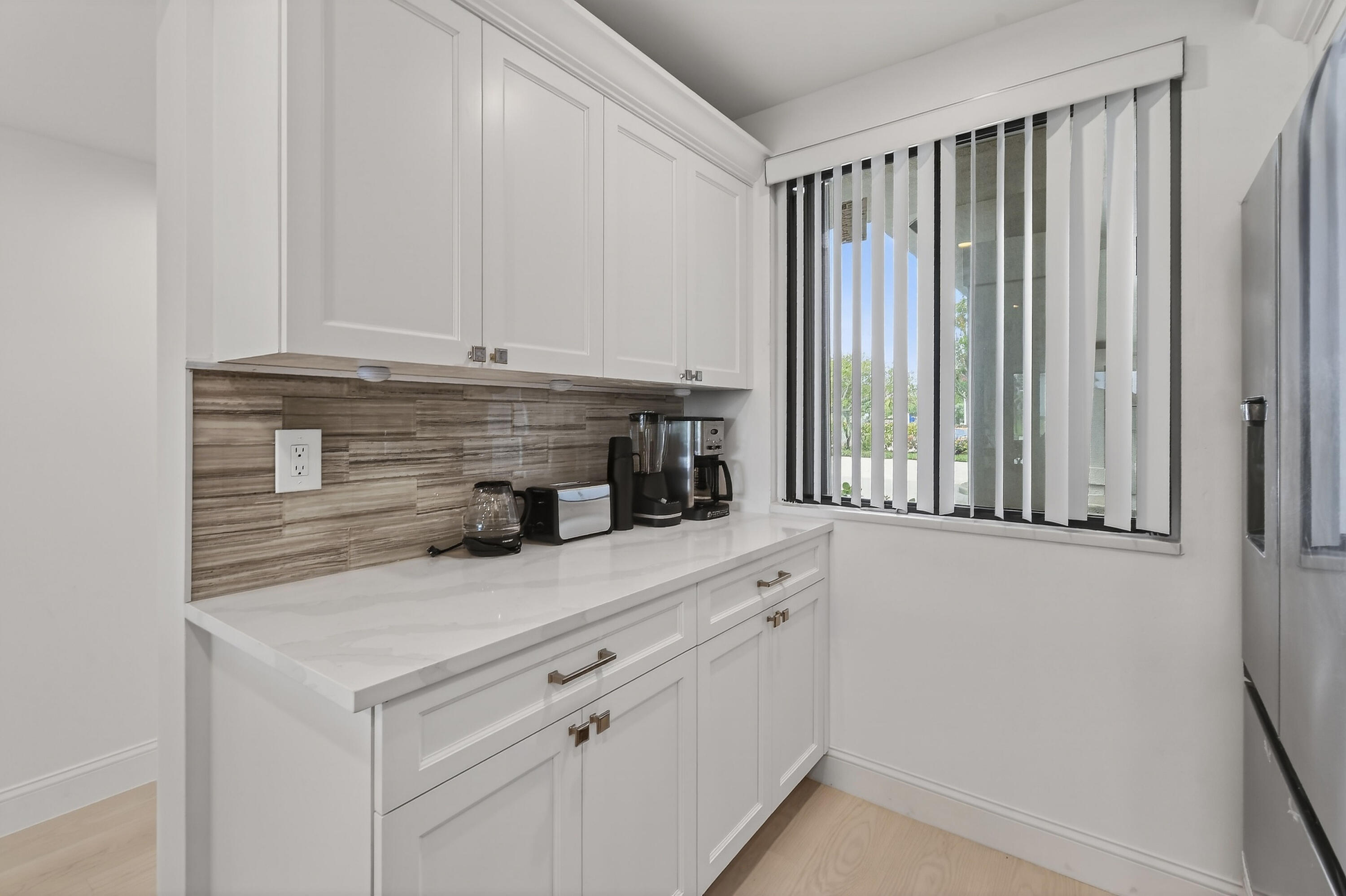 Kitchen with white cabinets, a wood-look backsplash, and a window with vertical blinds.