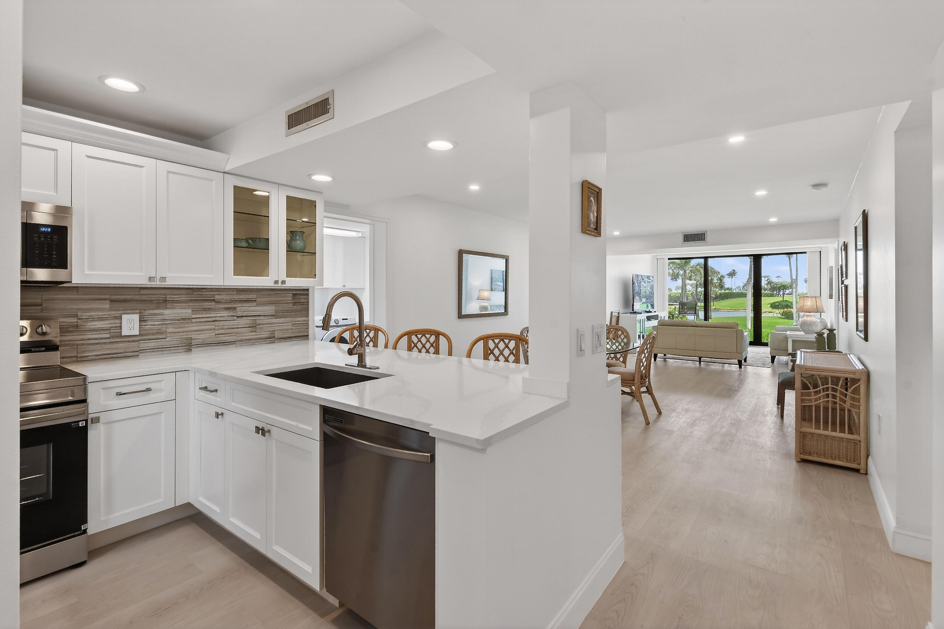 Open-plan condo kitchen with white island and living room opening through glass doors to a green lawn.