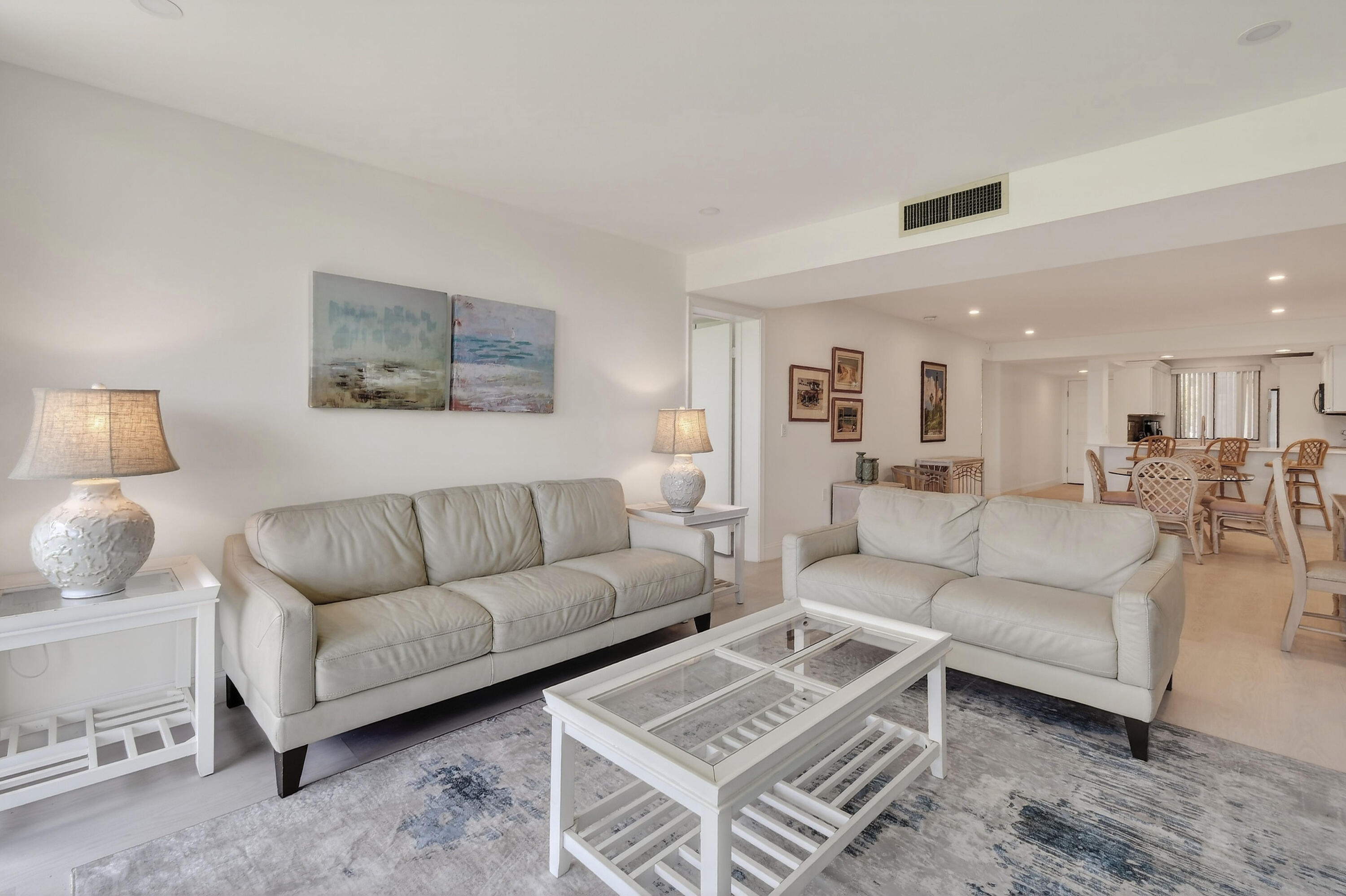 Furnished living room with two white sofas and a glass-top coffee table, opening to a dining area.
